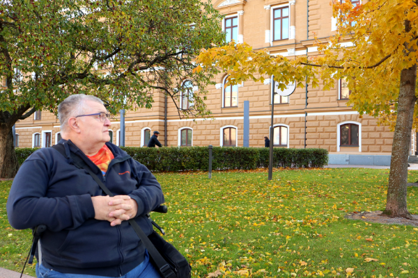 Pertti Latvala katselee sivulle puistossa, jossa puut alkavat kellastua syksyyn.
